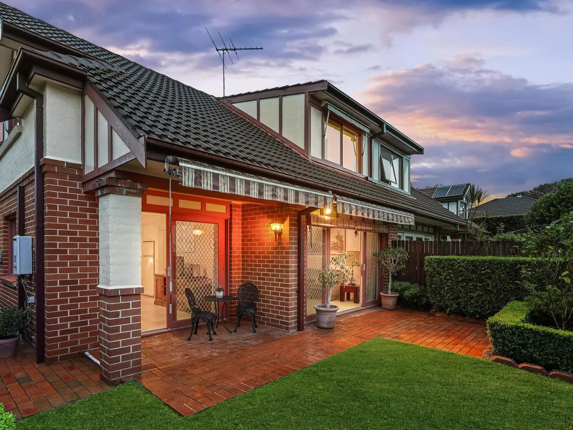 Brick house with an awning-covered terrace opening onto a courtyard lawn at dusk, Balgowlah