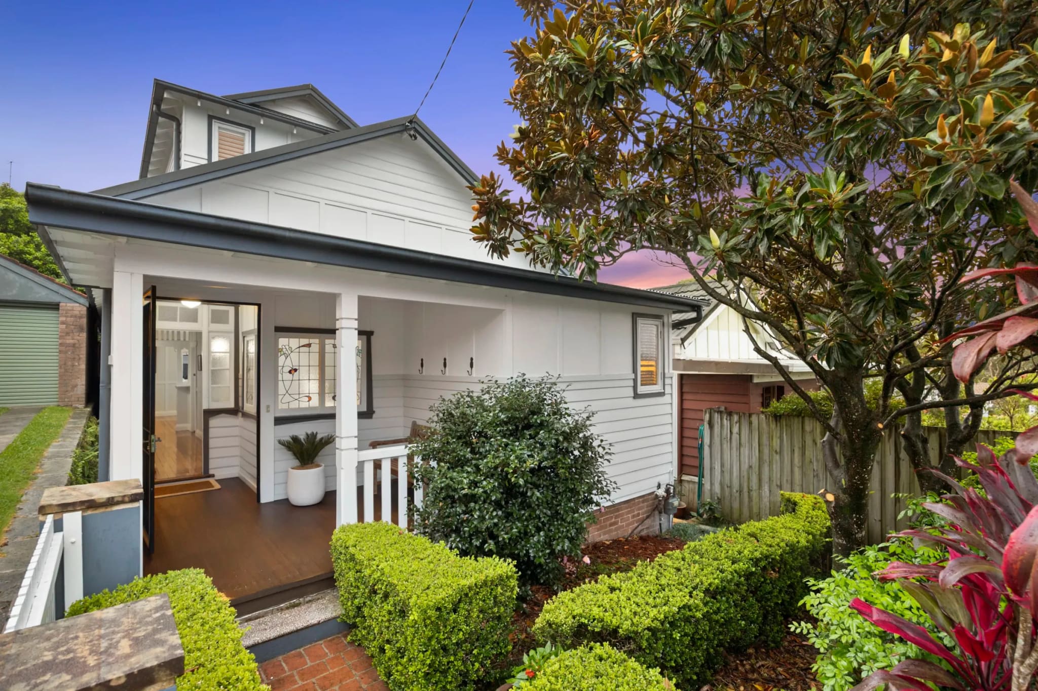 Weatherboard cottage with a white front verandah behind clipped hedges, Balgowlah