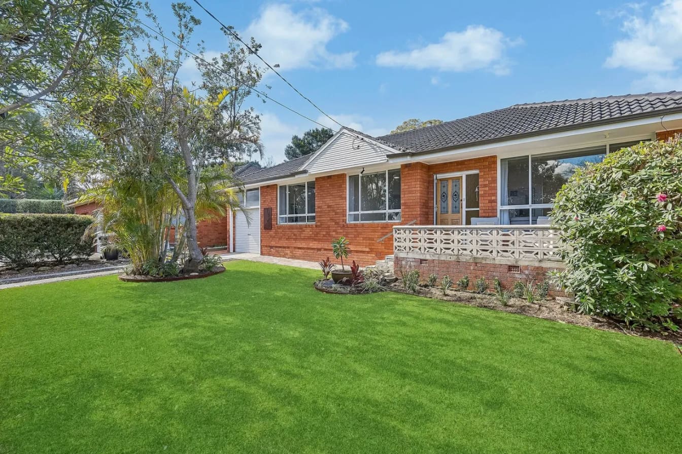 Red-brick house with a breeze-block front verandah behind a wide lawn, Frenchs Forest