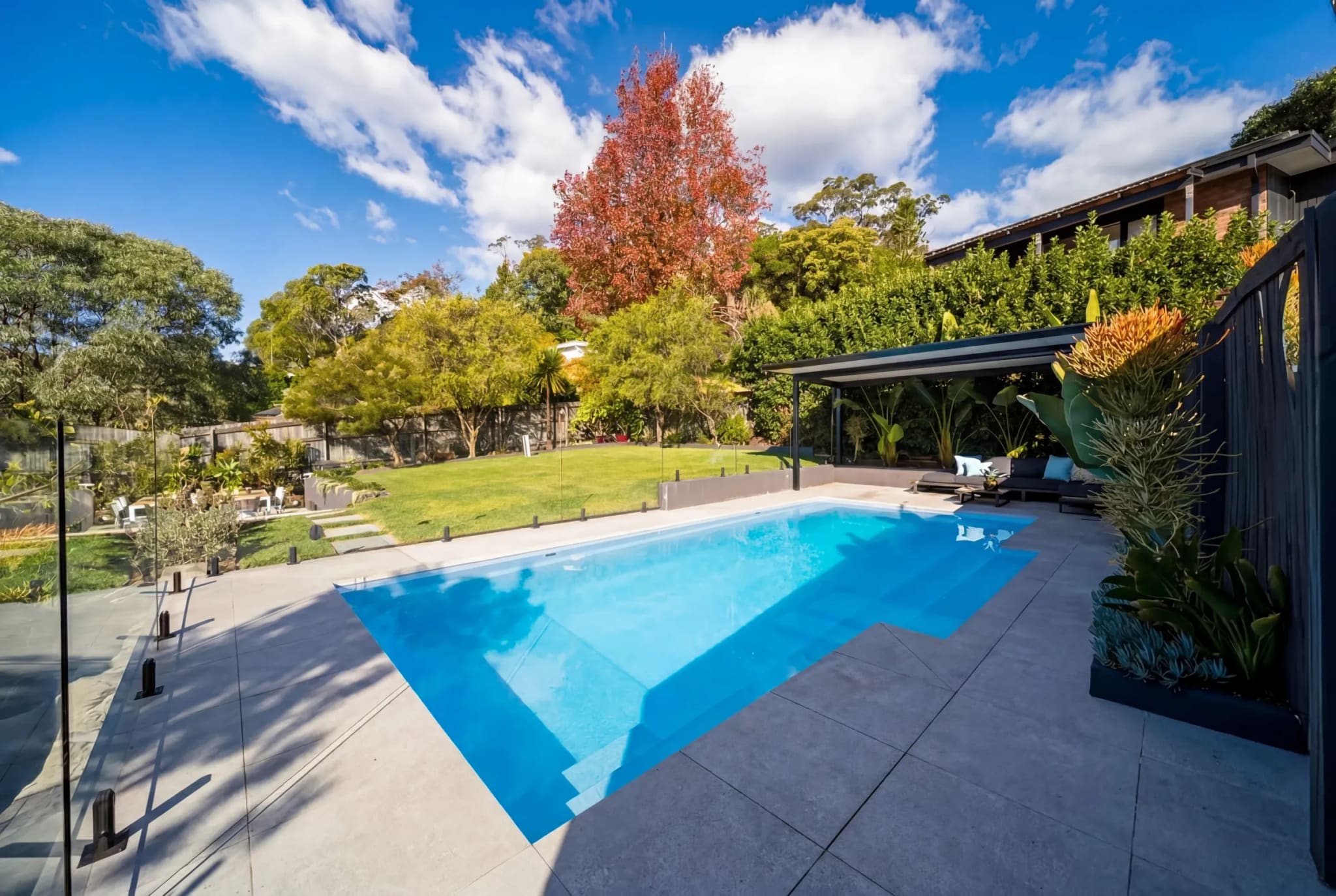 Pool and wide lawn behind a house, with established trees and a pergola, Frenchs Forest