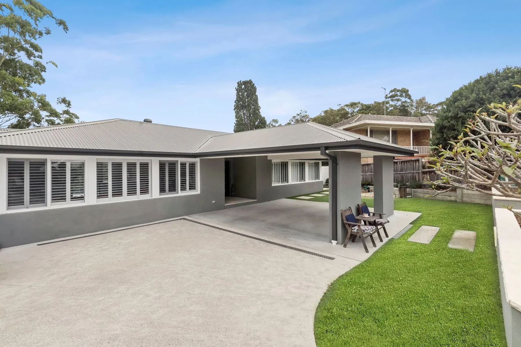 Single-storey rendered house with a carport and lawn, trees behind, Frenchs Forest
