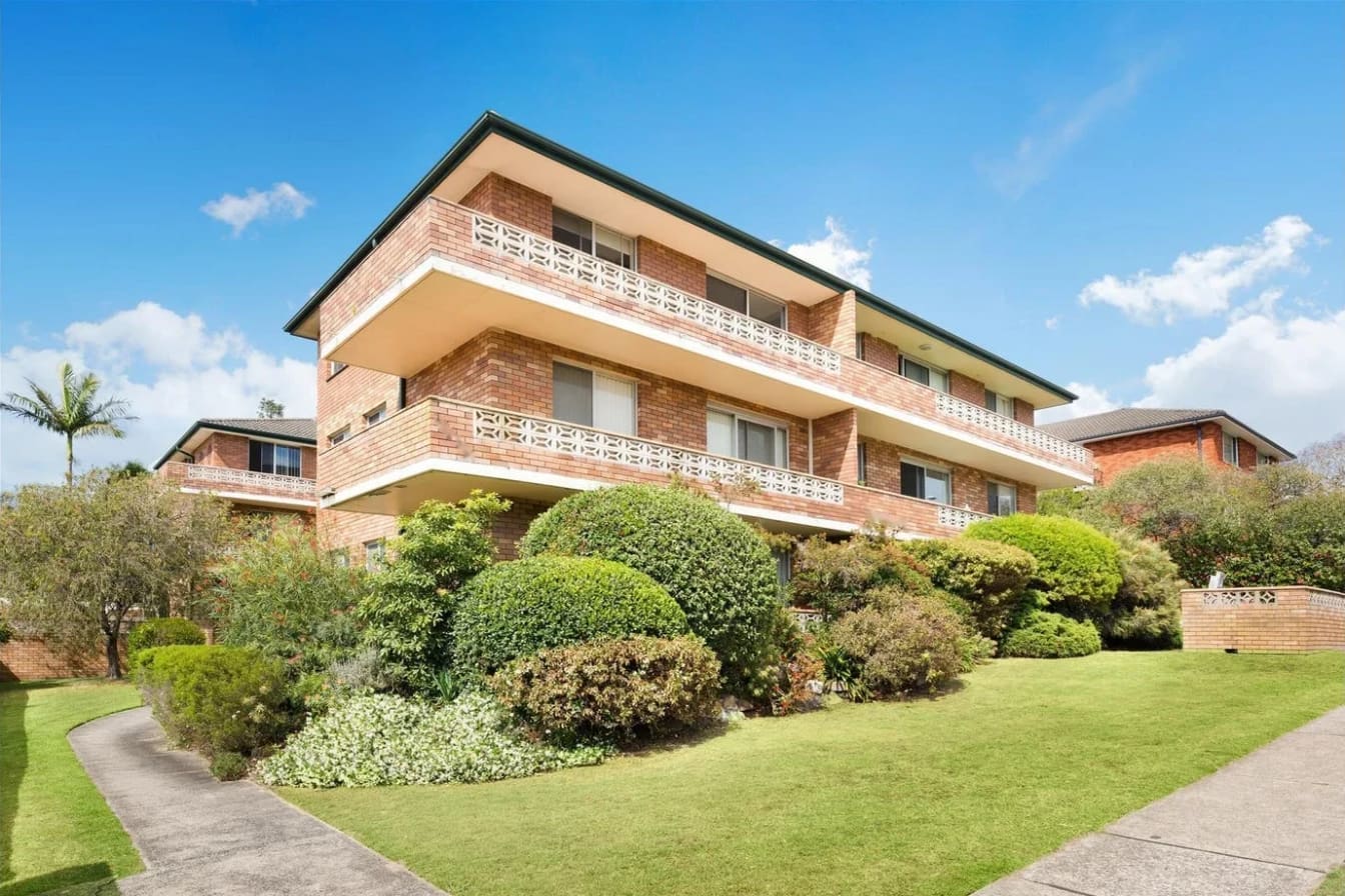 Three-storey brick walk-up with breeze-block balconies behind a garden and lawn, Freshwater