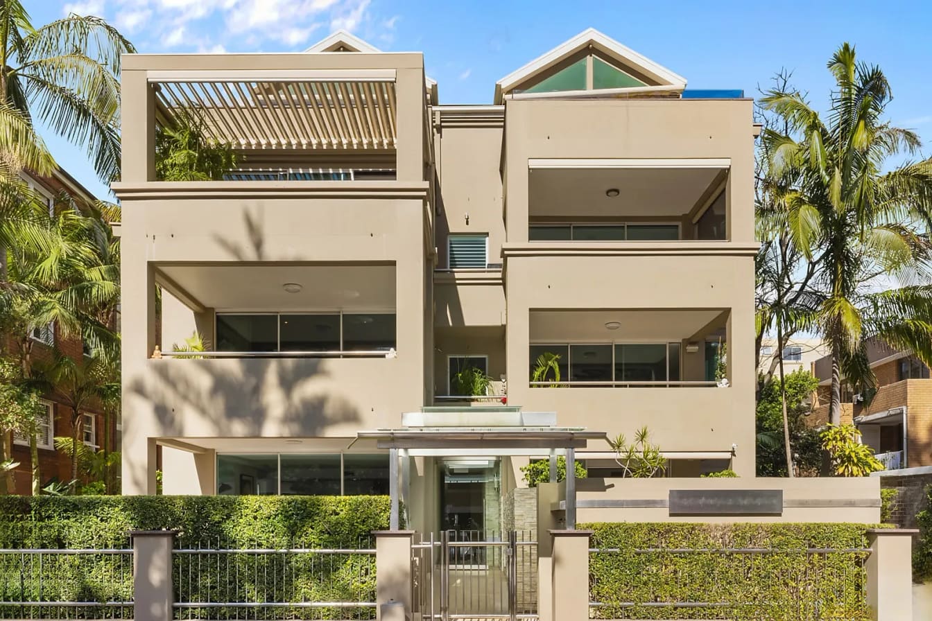 Three-storey rendered apartment block set behind palms, Manly