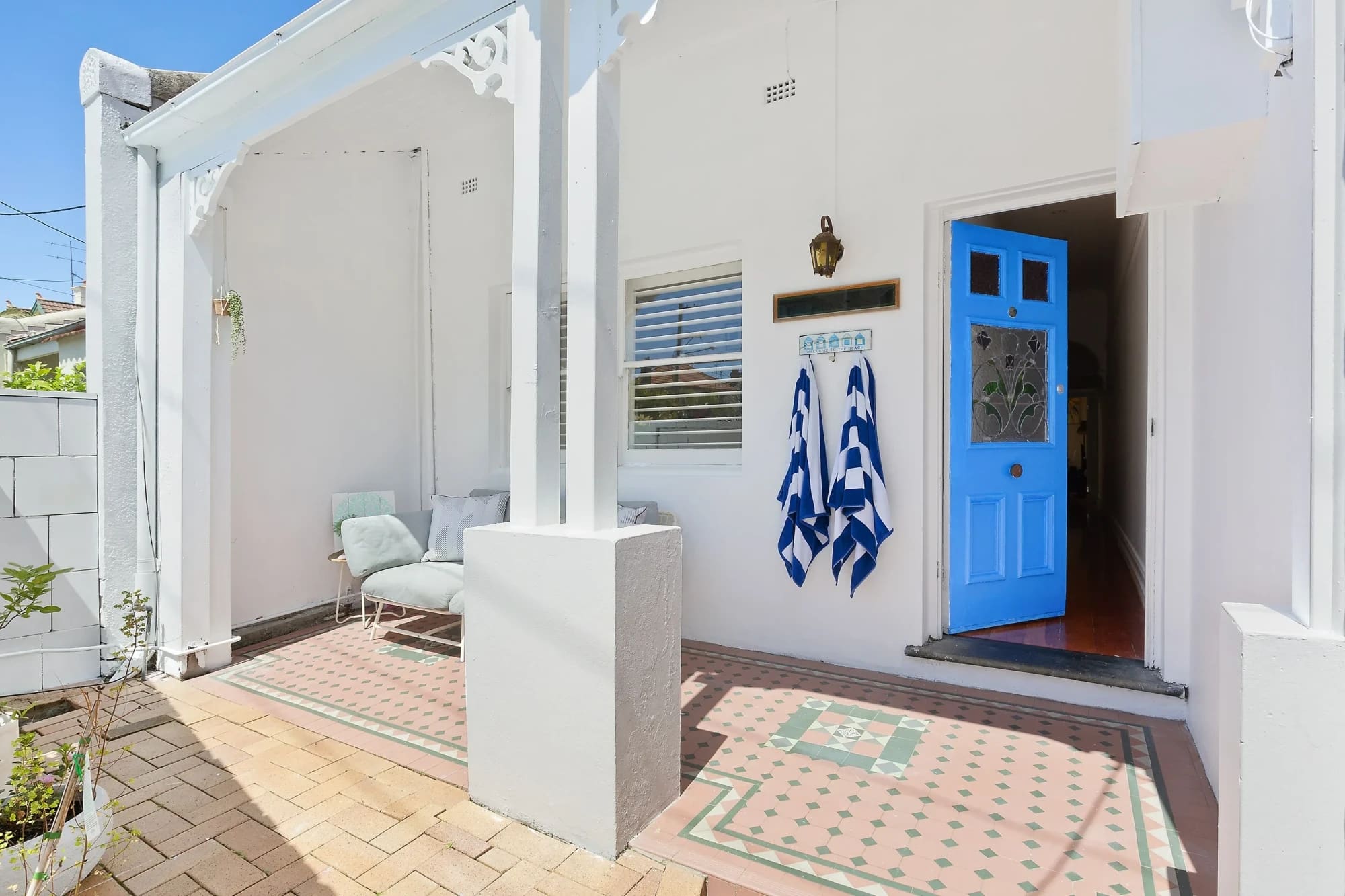 Tiled verandah and blue front door of a white weatherboard cottage, Manly